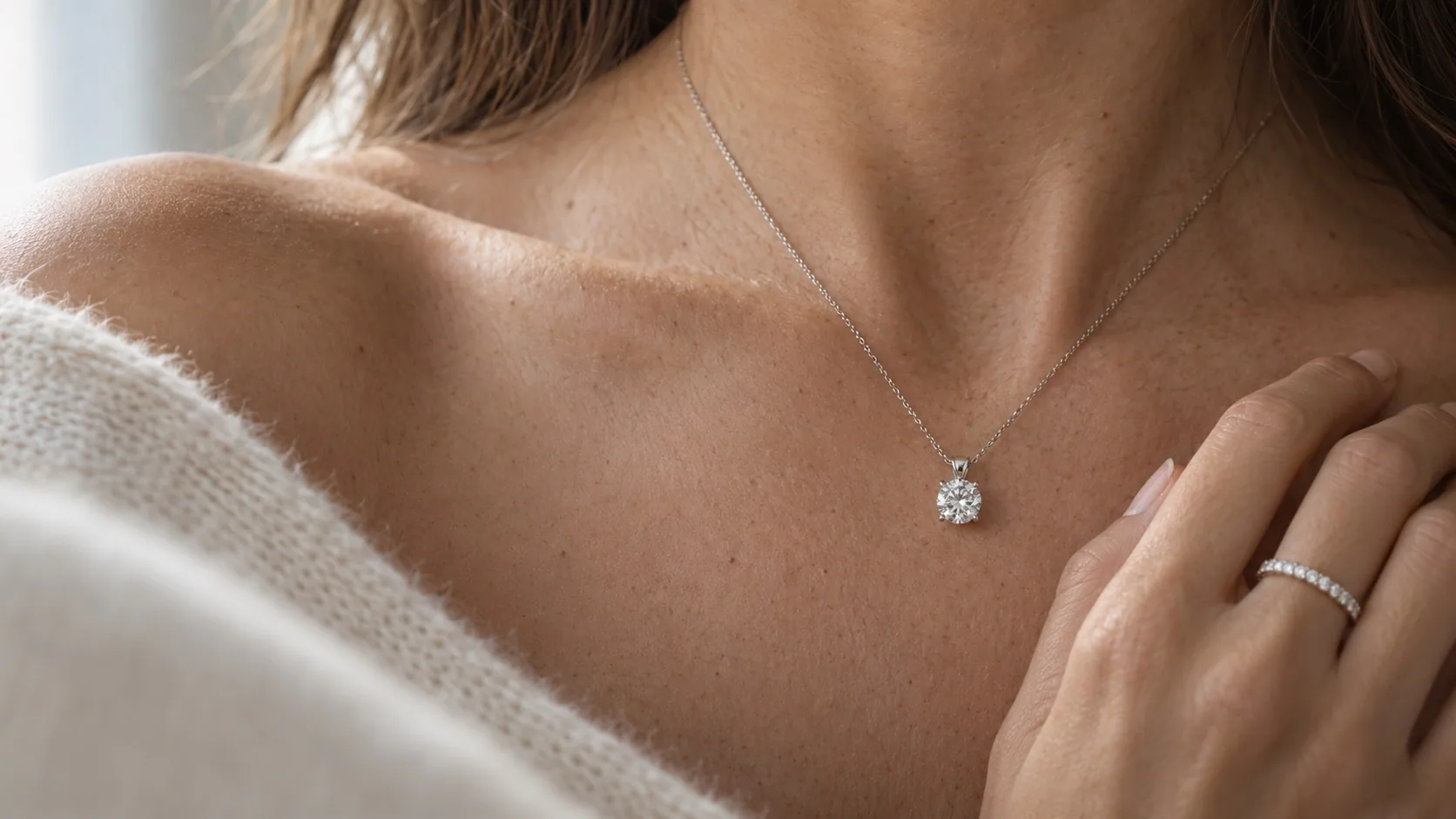 A round diamond solitaire pendant at the collarbone, with a diamond band on the hand