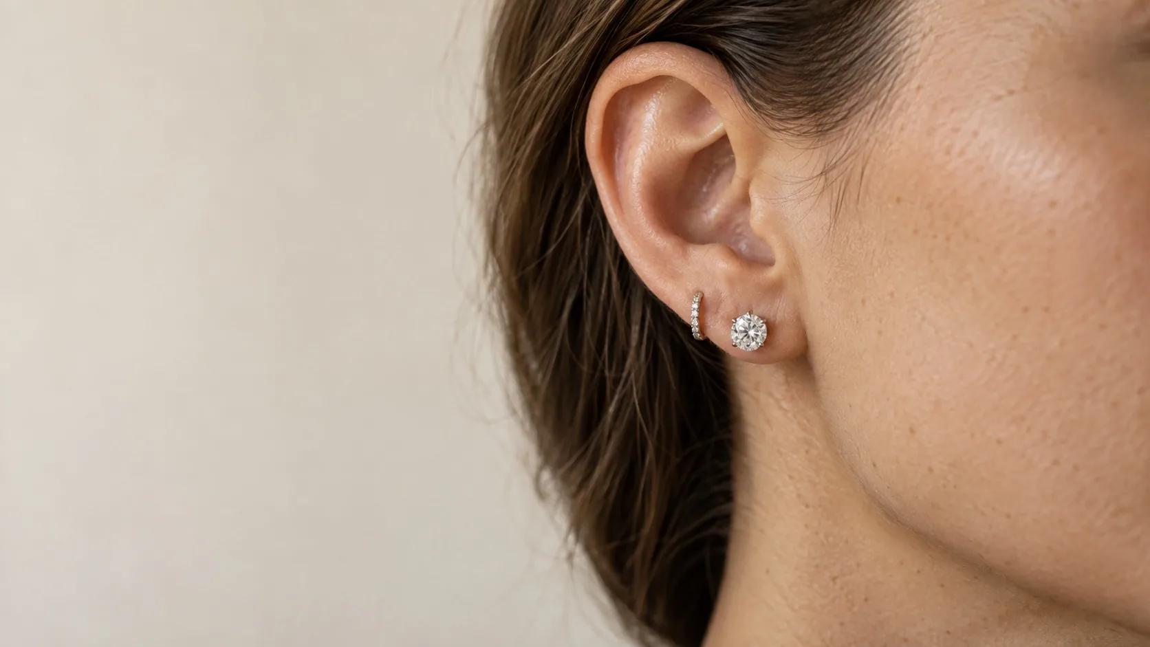 A round diamond stud and a small diamond hoop worn on the ear