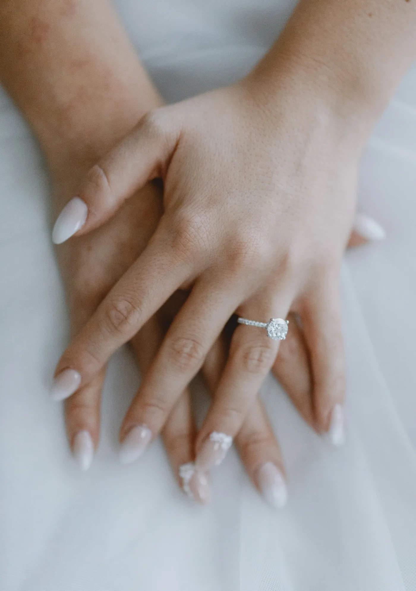 Crossed hands wearing a round diamond ring