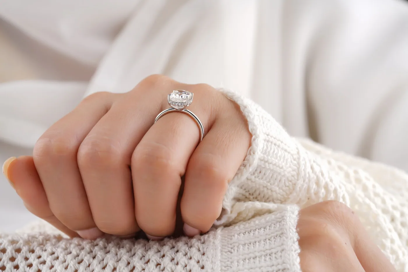 A diamond solitaire ring worn on a hand, cream knit sleeve