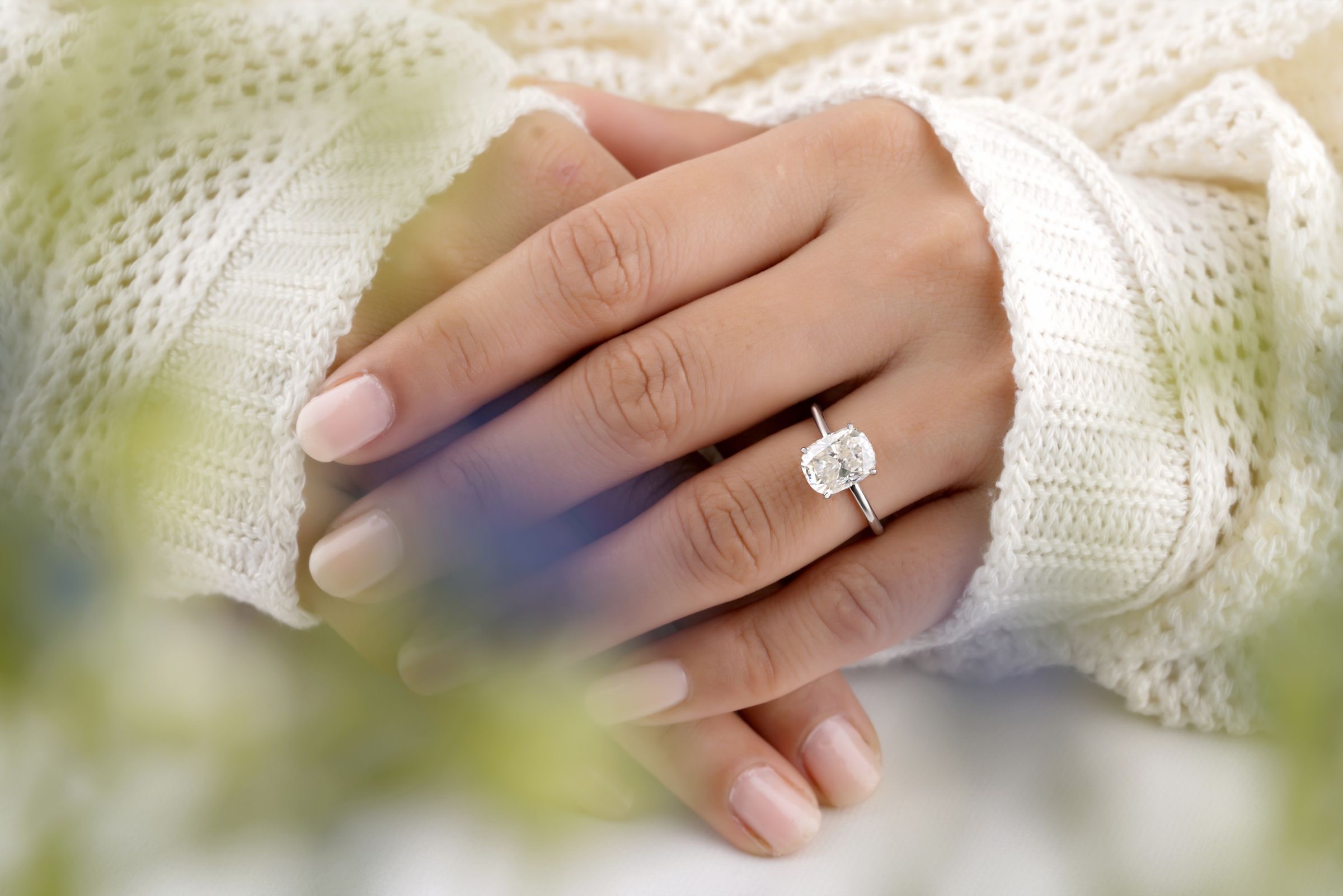 A diamond solitaire ring on folded hands in soft cream knit sleeves